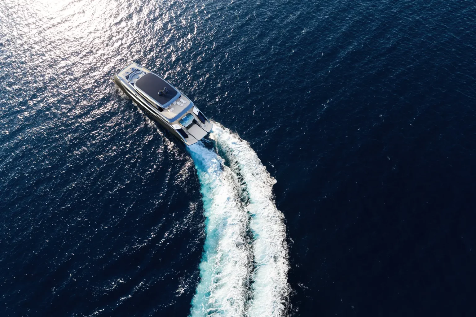 in Luftbild einer Sunreef Yacht, die mit hoher Geschwindigkeit durch das offene Meer fährt und dabei eine weiße Gischt hinter sich herzieht. Das tiefblaue Wasser reflektiert das Sonnenlicht und hebt die elegante Form des Schiffes hervor.