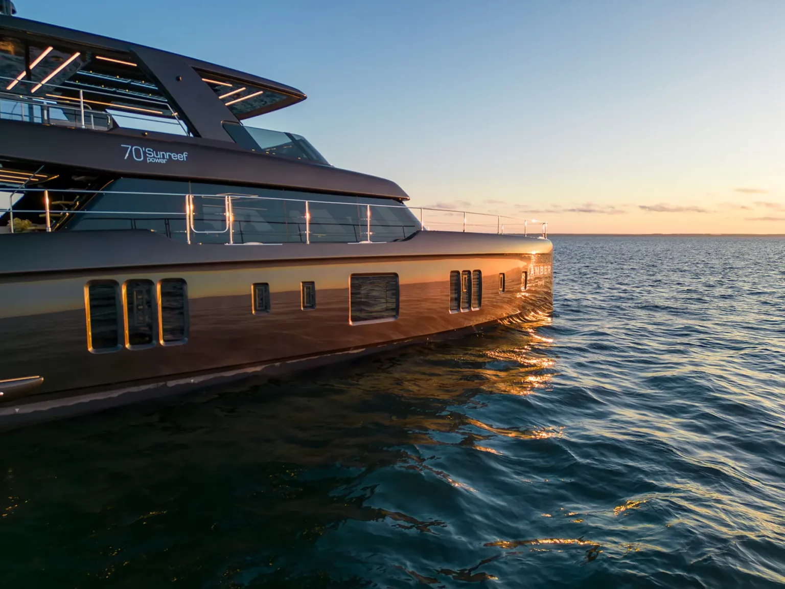 Seitlicher Blick auf die 70 Sunreef Power bei Sonnenuntergang, mit ihrem glänzenden, reflektierenden Rumpf, der das goldene Licht einfängt.