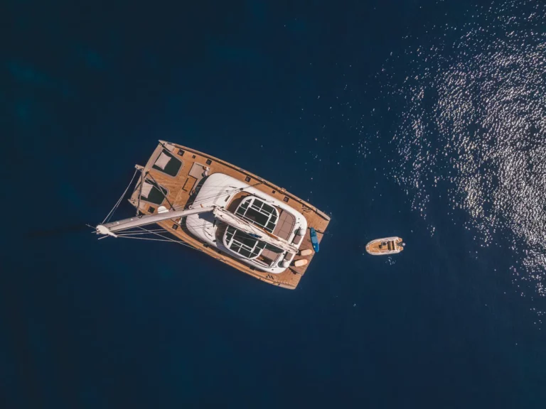 Luftaufnahme eines Sunreef 80 Katamarans auf dem offenen Meer, zeigt das weitläufige Deck mit Solarpanels und ein Beiboot neben der Yacht.