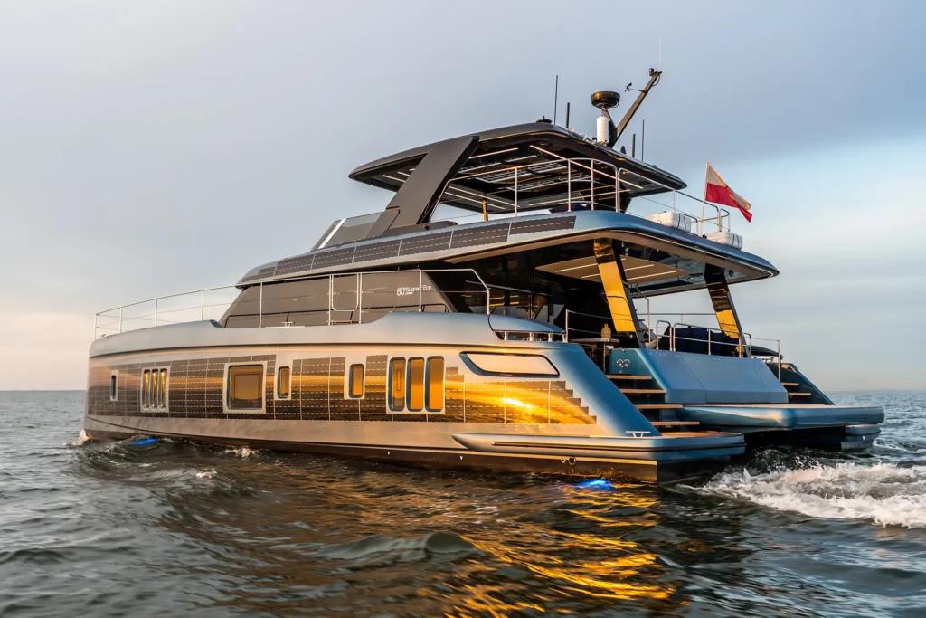 Das Bild zeigt eine luxuriöse Sunreef Power 60 ECO Yacht, die bei Sonnenuntergang über das Wasser gleitet. Die Yacht besticht durch ihr modernes Design mit eleganten Linien und ist mit Solarpanelen an den Seiten ausgestattet, die ihre umweltfreundliche Technologie unterstreichen. Die warmen, reflektierenden Lichtstrahlen auf der Wasseroberfläche betonen die stilvolle und nachhaltige Bauweise dieser innovativen Yacht.