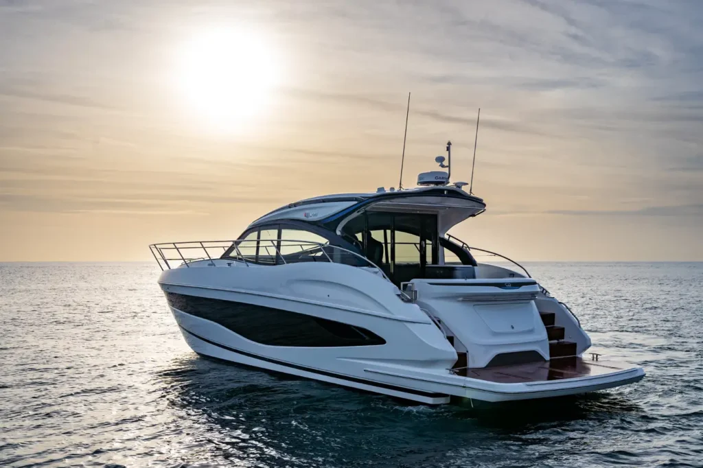 A sophisticated white v50 Princess Yacht viewed from the rear, illuminated by a golden sunset over the ocean