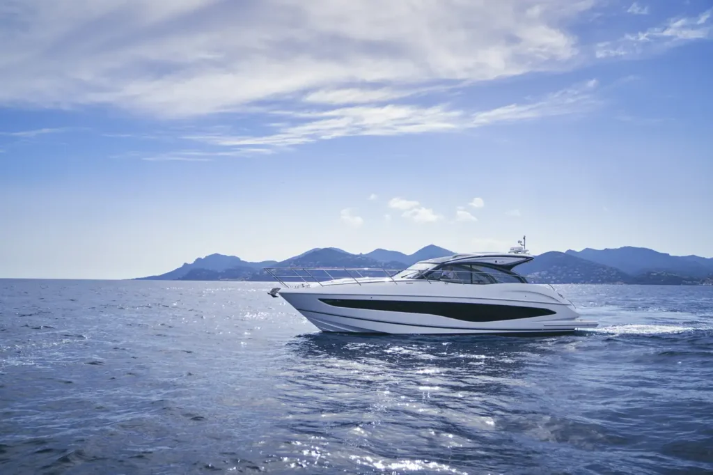 A modern white v50 Princess Yacht cruising on the sea with a backdrop of distant mountains and a bright sky