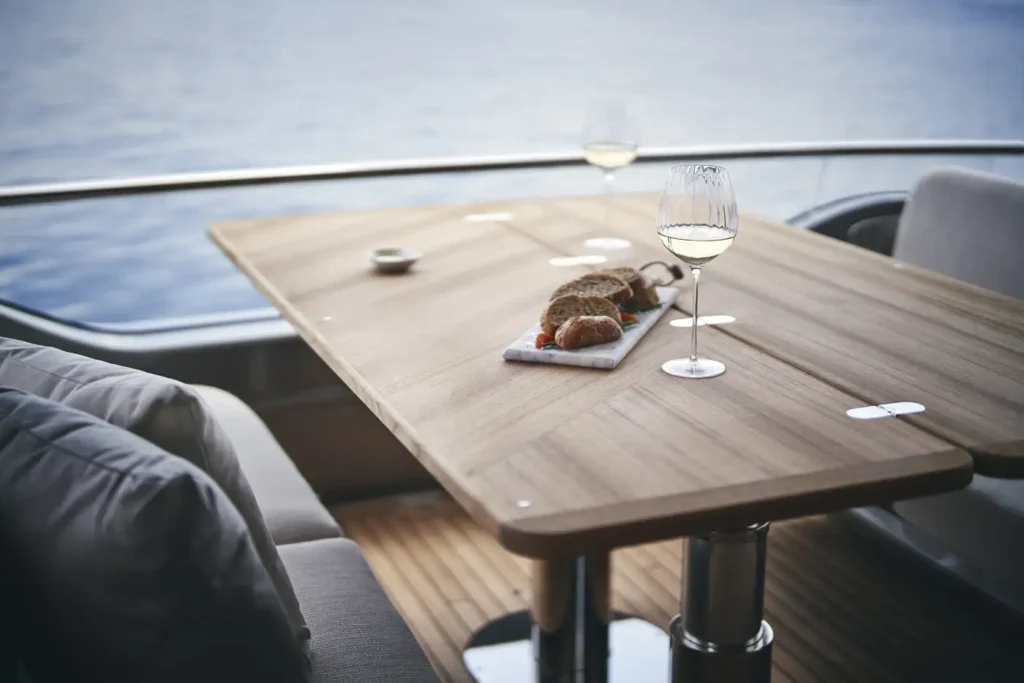 A luxurious dining setup on a y85 Princess Yacht, featuring a wooden table with a plate of bread and two glasses of white wine, overlooking calm blue waters