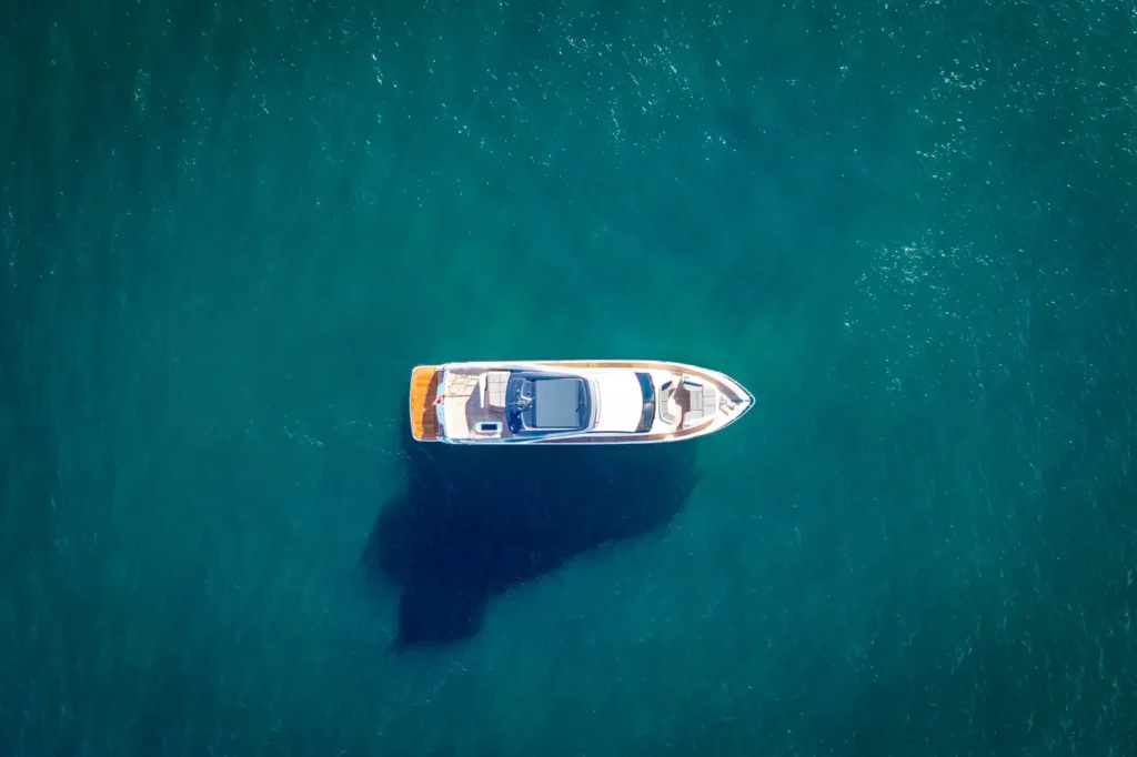 Aerial view of a sleek, modern y85 Princess Yacht floating in deep blue waters, with a distinct shadow visible beneath the vessel